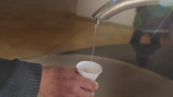 Therapeutic mineral water flows from the tap into a paper cup held by a man's hand. The healing water pours smoothly, video