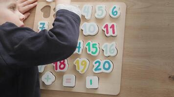 the boy learns to count, holds a board with numbers-puzzles arranged in order from 1 to 20, the boy is 4-5 years old European appearance, at home sits at the table, preparation for school video