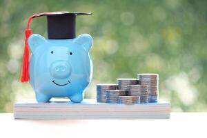 Graduation hat on piggy and stack of coins money on natural green background photo