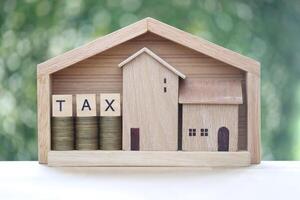 Tax concept,Small house in big house with stack of coins money and tax word on green background photo