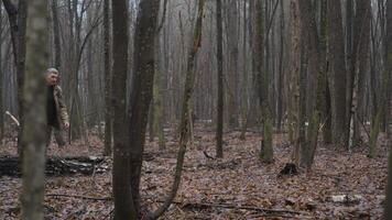 A man walks through a dense forest with a backpack and an axe, surrounded by tall trees and fallen leaves on a foggy autumn morning, enjoying nature. video