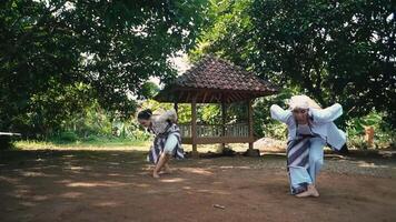 Two individuals performing a traditional dance in a rural setting, surrounded by greenery. They are dressed in traditional attire, showcasing cultural expression video
