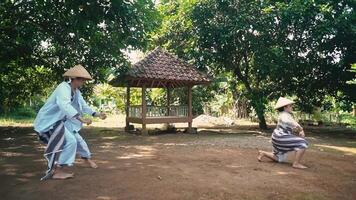 Two individuals performing a traditional dance in a lush green outdoor setting, showcasing cultural attire and movements. A gazebo is visible in the background, surrounded by trees video