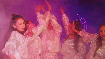 A vibrant group of young people in shiny silver outfits dancing in a colorful, smoky environment. The scene is illuminated with neon lights, creating a lively atmosphere video