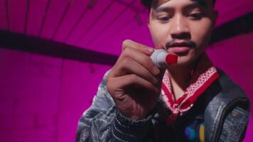 A young man in a leather jacket and bandana is writing with a red marker on a transparent surface. The background features vibrant pink lighting, creating a dynamic atmosphere video