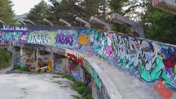 Sarajevo, Bosnia and Herzegovina 08-26-2024, Abandoned bobsleigh track in Sarajevo. Drone view of the track curve immersed in the forest and painted with graffiti. 1984 Sarajevo Winter Olympics video