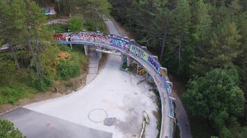Sarajevo, Bosnia and Herzegovina 08-26-2024, Aerial view of abandoned bobsleigh track in Sarajevo. Drone view of the track curve immersed in the forest and painted with graffiti. Winter Olympics video
