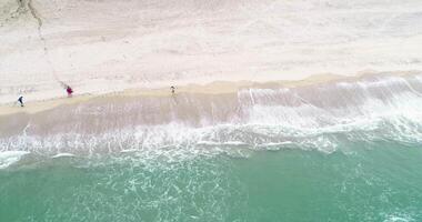 people walking on the shore of a beach a cloudy day, aerial footage from drone video
