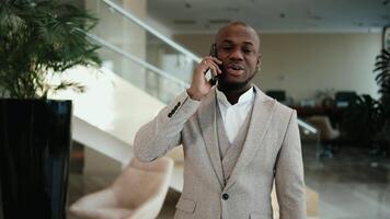 An African American CEO businessman talks on the phone in a modern office hallway. Concept dynamic work environment, professionalism, and effective communication video