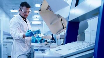 Male scientist analyzes a blue liquid in a laboratory. Test tubes with liquid and pipette pouring substance in modern laboratory with advanced equipment. video