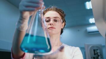 A scientist analyzes a blue liquid in a modern laboratory, close-up in a flask, examining it. A conceptual study using the latest technology to analyze chemicals video