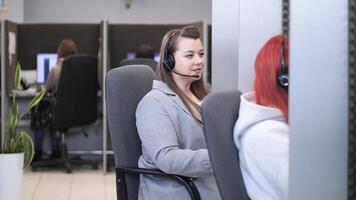 Female call center operator talking with client using headset in busy office video
