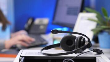Headset lying on desk, office worker typing in background video