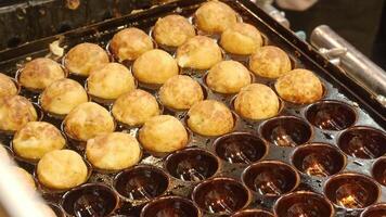 Japanese Takoyaki cooking. A street food chef preparing freshly cooked takoyaki. Japan Takoyaki made of batter filled with diced octopus and served hot. Chef places the golden Tako ball in a tray video