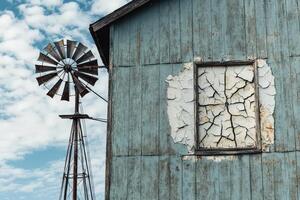 An old blue house with a cracked window and a windmill photo