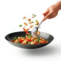 A person's hand is holding a fork and stirring food into a wok photo