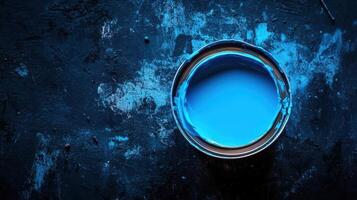 A tin of vibrant blue paint sits on a dark surface photo