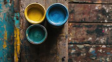 Three paint cans rest on a weathered wooden surface photo