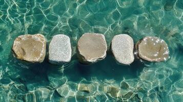 Five smooth stones submerged in clear teal water photo