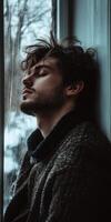Lonely man sitting by the window lost in thought on a rainy day photo