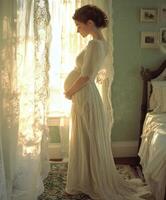 Expecting mother in elegant gown in softly lit bedroom photo