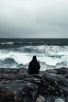 A person sitting on a rock overlooking the ocean photo