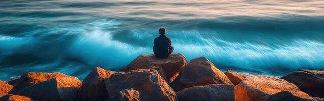 Sitting on rocks by the ocean at sunset contemplating the waves photo