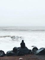 Person sitting on rocks by the ocean on a foggy day photo