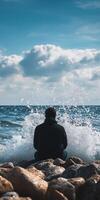 Man sits on rocks by the ocean enjoying the waves in daylight photo