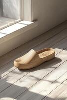Wooden clogs positioned near a sunlit window on a wooden floor photo