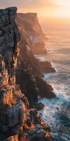 A rocky cliff with waves crashing into the ocean at sunset photo