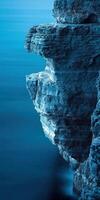 A rock face in the ocean with a blue sky photo