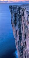 A cliff edge with a blue sky and water photo