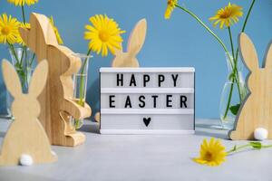 Happy Easter text on Lightbox with bunny wooden figures and fresh flowers. Easter composition content still life. Christian symbols of spring holiday photo