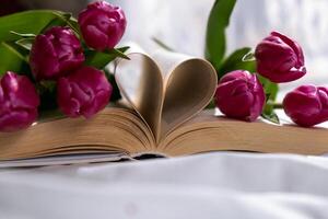 Book pages in shape of heart symbol love with bouquet of pink tulips on messy bed. Romantic morning scene. Greeting card Holiday flowers springtime atmosphere photo