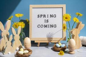 SPRING IS COMING text on letter board with bunny wooden figures and fresh flowers. Easter composition content still life. Christian symbols of spring holiday photo