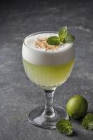Refreshing Pisco Sour Cocktail with Lime and Mint Garnish on Dark Surface photo