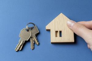 House Keys and Wood Home in Hand on Blue Background Concept photo