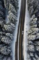 Driving on Snowy Road Through Winter Forest From Above with Car photo