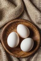Three White Eggs in Wooden Bowl on Beige Lace Background photo