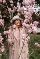 Woman magnolia flowers, surrounded by blossoming trees., hair down, white hat, wearing a light coat. Captured during spring, showcasing natural beauty and seasonal change. photo