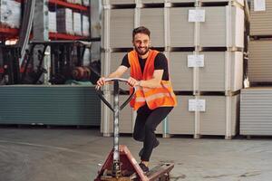 Standing with platform trolley. .Storage worker is in the warehouse with bunch of products photo