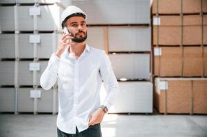 Using phone.. Storage worker is in the warehouse with bunch of products photo