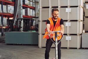 Having fun by riding platform trolley. Storage worker is in the warehouse with bunch of products photo