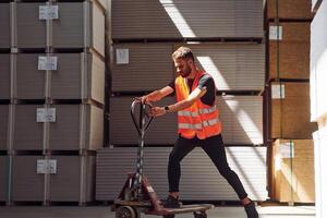 Riding the platform trolley. Storage worker is in the warehouse with bunch of products photo