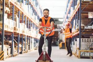 Having fun by using trolley platform. .Two storage workers is in the warehouse photo