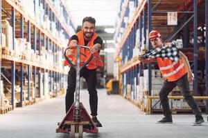 Man riding trolley platform. ,Having fun. Two storage workers is in the warehouse photo