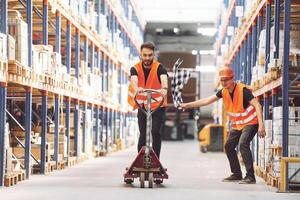 Man riding trolley platform. Having fun. Two storage workers is in the warehouse photo