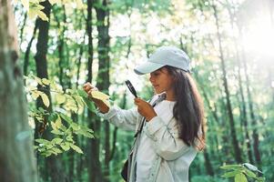 With magnifying glass. .Girl is in the forest at summer day time discovering new places photo