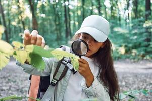 Using magnifying glass. Girl is in the forest at summer day time discovering new places photo